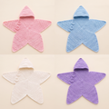 Four hand-crocheted five-point star baby wraps in blush pink, powder blue, cream and lilac, laid flat on a warm cream background